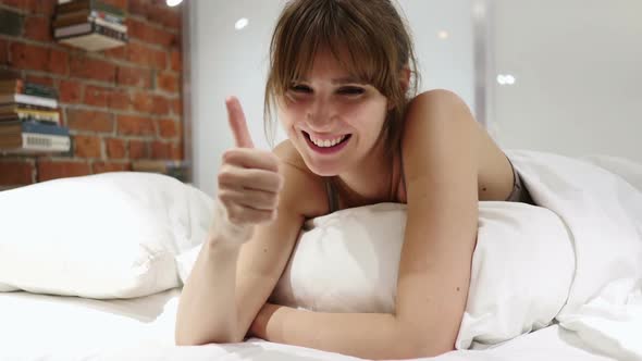Thumbs Up By Happy Woman Lying in Bed on Stomach
