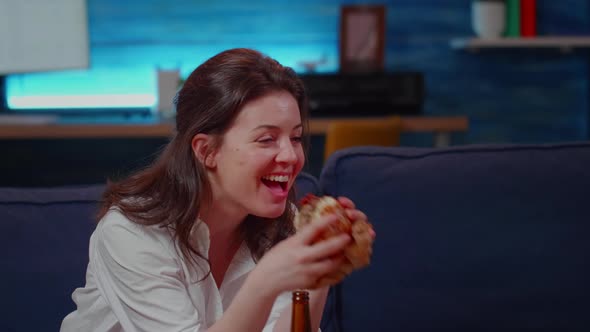 Young Person Laughing at TV While Eating Hamburger