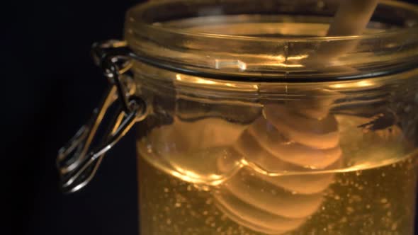 Stirring golden runny honey in a glass jar with honey drizzle spoon medium shot