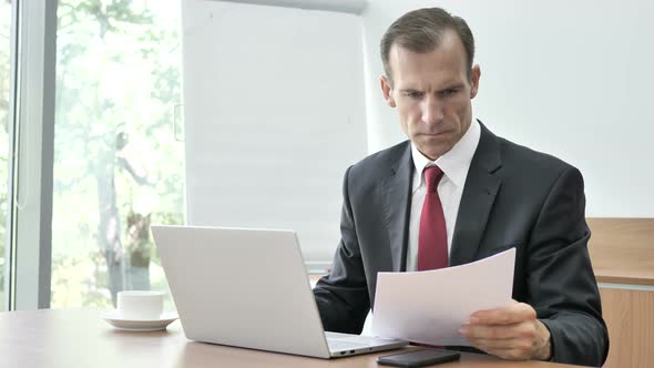 Businessman Reading Documents and Working on Laptop Paperwork