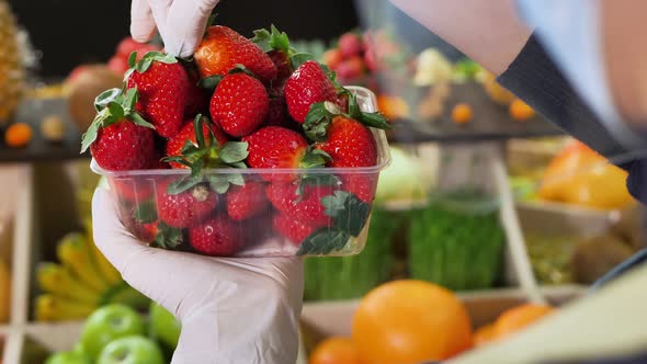 Closeup of Strawberries in a Tray in the Hands of a Salesman Wearing Gloves and a Mask During