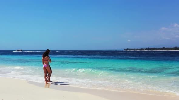 Young couple standing on white sand of exotic beach, watching beautiful sea waves splashing on their