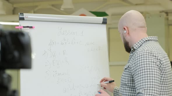 Teacher Records Video Lessons He Stands and Writes with a Pen on a Flip Chart