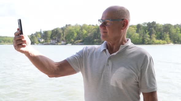 Happy Senior Man Taking Selfie With Phone By The Lake