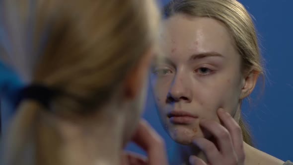 Young Crying Girl Looking at Face Acne in Mirror, Suffering From Skin Problems