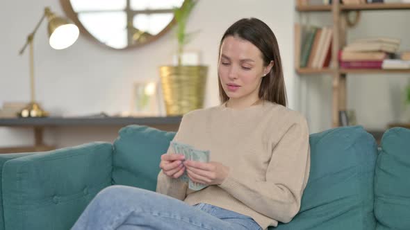 Successful Young Woman Counting Dollar on Sofa 