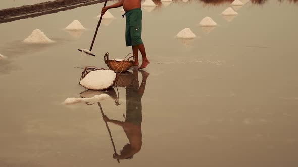 Low section shot of a salt field worker harvesting salt in Kampot, Cambodia