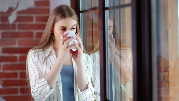 Adorable Smiling Young Business Woman Drinking Tea or Coffee and Looking Out Window