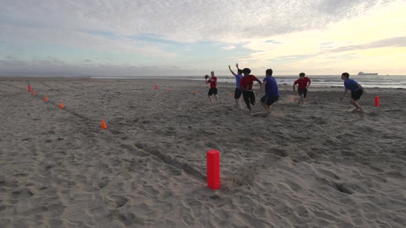 A group of guys playing flag football on the beach.