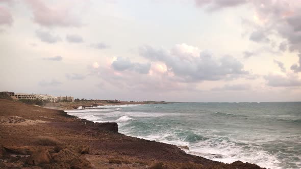 View From the Shore of Large Sea Waves Crashing Against Rocks on a Cloudy Day