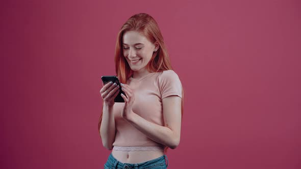 The Young Woman with Red Hair with the Phone in Her Hand Thinks Then Types a Message and Smiles
