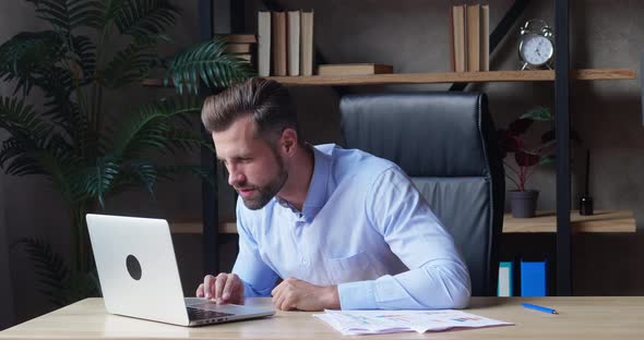 A Businessman in a Blue Shirt Looks at the Laptop Screen with Concentration and Expresses an Emotion