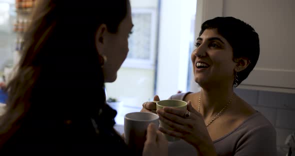 Happy girl friends lesbian couple enjoying a cup of tea or coffee in their new home