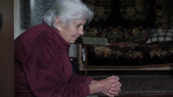 Side View An Elderly Caucasian Woman With Tremor With Gray Hair Sits On A Chair