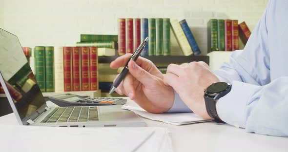 Male Hands with a Pen Closeup  Man Thinking on the Workplace in Front of Laptop Monitor