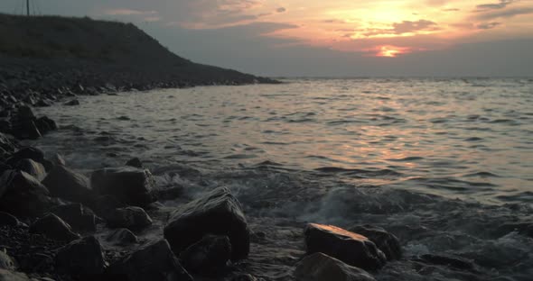 Wide Angle Beach at Sunset with Sun Reflected on Ocean and Waves Splashing Against Rocks