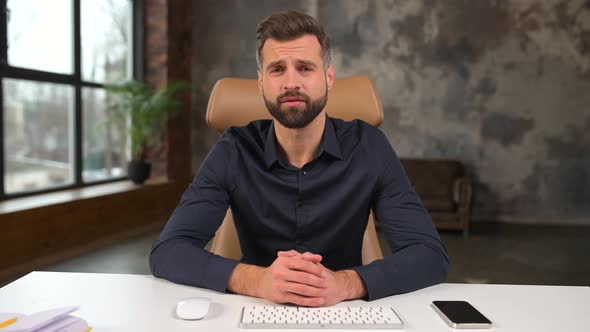 Smiling Bearded Caucasian Businessman Sitting at the Desk and Looking at the Camera While Waving