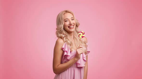 Blonde Lady Eating Lollipop Having Fun Posing Playfully Pink Background