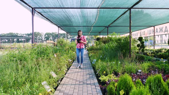 Female Gardener Checks Quality of Plants, Takes Notes on Digital Tablet, Walking Along Garden Center