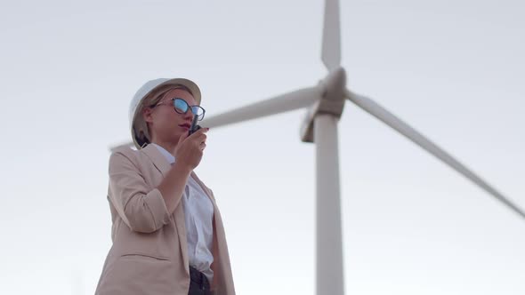 Beautiful Woman Engineer Talking on the Walkie - Talkie and Looks at the Wind Generator, Solid Woman