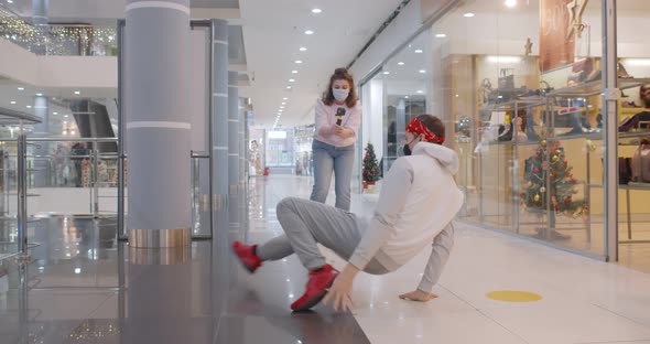 Young Woman in Face Mask Recording Dance Moves of Male Breakdancer at Camera