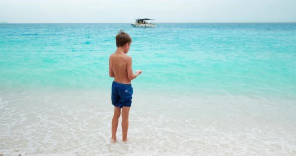 Young boy throwing rocks in the sea at the beach.