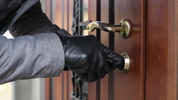 a thief in gloves opens the door lock of a private house and penetrates inside