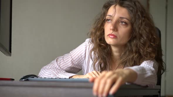 Tired Young Woman with Curly Hair and White Shirt is Working at the Office Using Her Laptop Routine