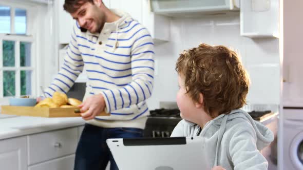 Father talking on mobile phone while son using digital tablet