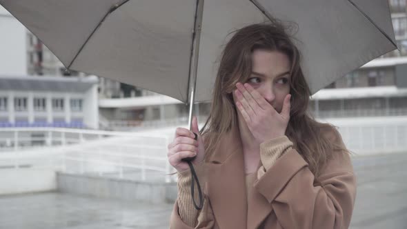 Young Ill Caucasian Woman Couching As Standing Outdoors Under Rain and Waiting. Portrait of Brunette