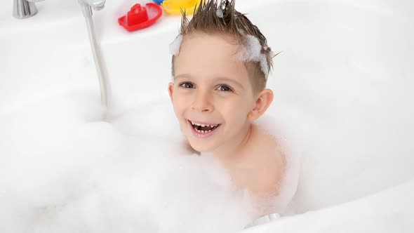 Portrait of Happy Smiling Boy Washing in Bath with Soap Suds and Looking in Camera