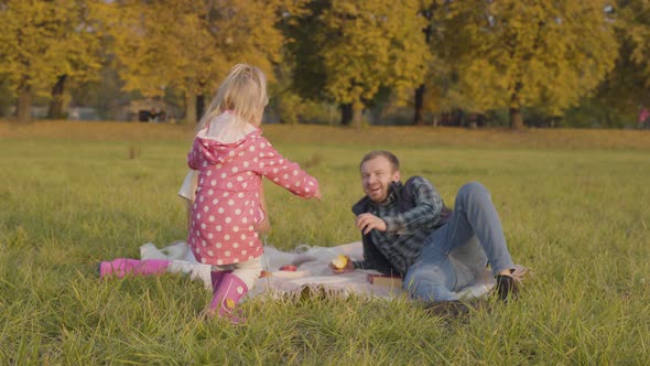 Little Blonde Child Dressed in Pink Clothes Walking To the Elder Sister and Father Sitting