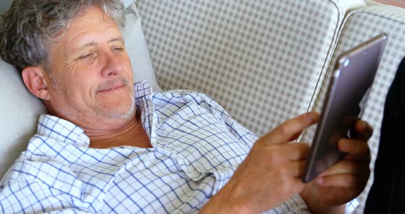 Senior man with digital tablet lying on sofa on the porch 4k