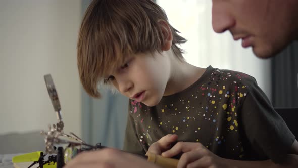 Father Teaching His Little Son to Solder Electronic Contacts at Home