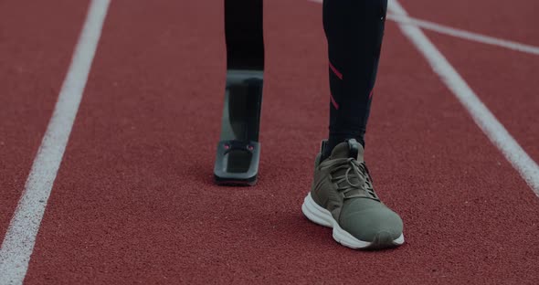 Crop View of Disabled Male Person with Prosthetic Running Blade Walking and Stopping at Sports Field