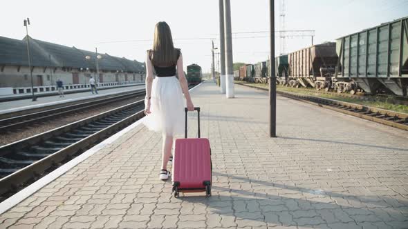 Pretty Girl Walks with Suitcase on Platform and Waving Her Hand to the Train
