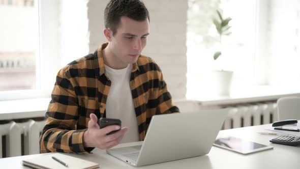 Casual Young Man Using Smartphone at Work
