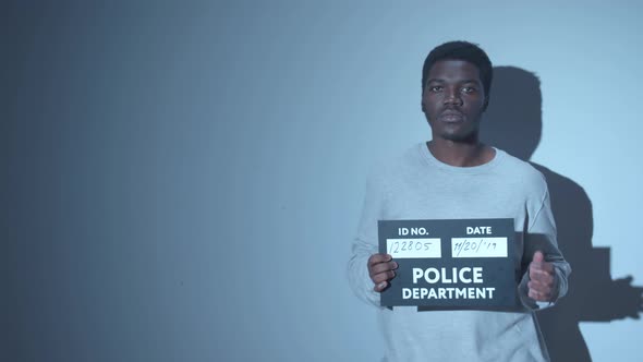 Black Criminal Holds a Sign for a Photo in the Police