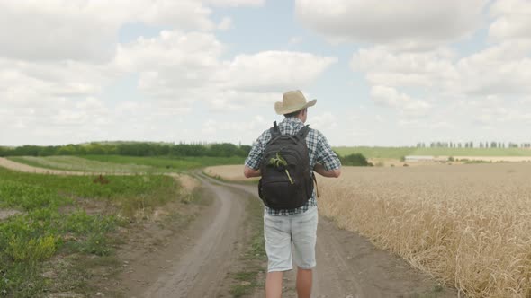 Rear view of hike of brave Caucasian guy with backpack walks along country road