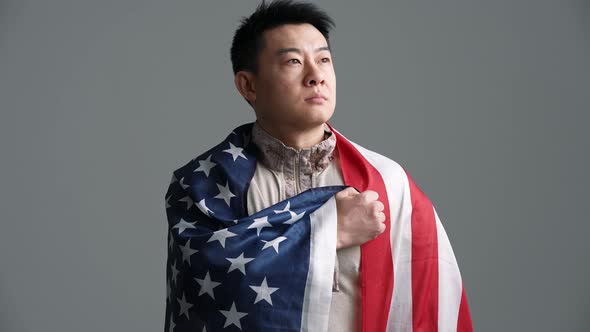 Confident soldier Asian man covered with the USA flag takes an oath