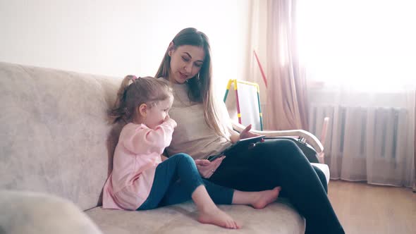 Mother and Daughter Are Sitting on the Couch and Teaching Using a Tablet Computer