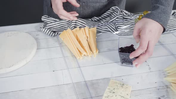 Step by step. Arranging cheese platter with fresh fruits, gourmet cheese, and crackers.