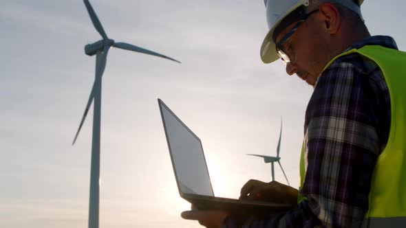 Windmill Engineer Watching Wind Turbines in Operation on a Laptop