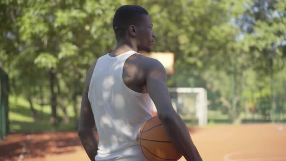 Back View of African American Sportsman in White Shirt Standing with Ball on Sunny Basketball Court