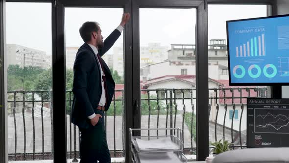 Businessman Sitting Near the Big Windows of His Office Looking Outside and Thinking