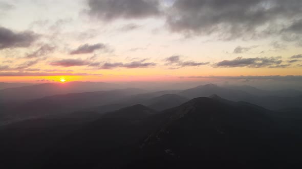 Aerial View of Foggy Evening Over High Peak with Dark Pine Forest Trees at Bright Sunset