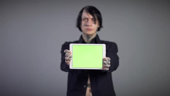 Closeup White Tablet with Green Screen in Tattooed Male Hands with Blurred Young Man at Grey