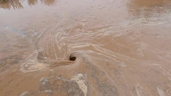 Muddy flood water sucked into the ground in whirlpool
