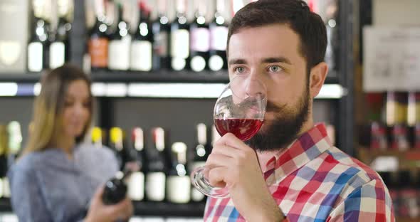 Close-up of Handsome Confident Caucasian Man with Beard Tasting Red Wine From Glass. Professional