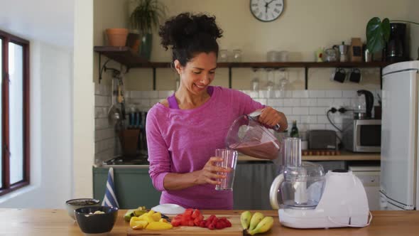 Portrait of mixed race woman pouring fruit juice in a glass from juice maker in the kitchen at home